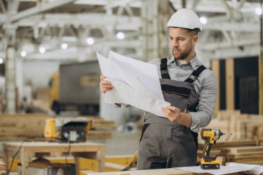 İnşaat işçisi modüler yapı fabrikasının planlarını inceliyor, doğru prefabrikasyonu ve montajı sağlıyor.