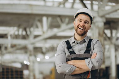 Çapraz kollarla gülümseyen neşeli bir mühendisin portresi modern bir modüler yapı fabrikasında güven ve uzmanlık sergiliyor.