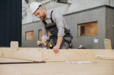 Marangoz, prefabriksiyon endüstrisinde modüler yapı için kablosuz matkap ve ahşap çerçeve kullanarak güvenlik kaskı takıyor.