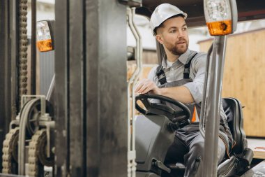 Yetenekli bir depo işçisi fabrikada forklift kullanıyor ve verimli kargo taşımacılığına odaklanıyor. Gelişmiş teknoloji üretimdeki yenilikleri ön plana çıkarıyor