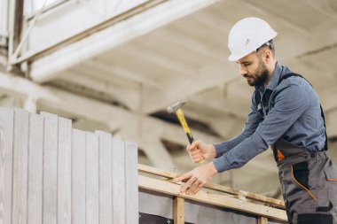 Marangoz ahşap tahtalara çivi çakıyor, fabrika ortamında prefabrik evler inşa ediyor.