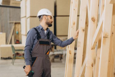 Marangoz, işlek bir atölyede ahşap bir yapı iskelesini inceliyor, imalatta zanaat ve profesyonellik sergiliyor.