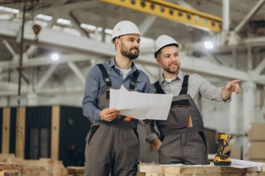 Planları inceleyen ve bir modüler yapı fabrikasında inşaat yapmayı planlayan iki mühendis, ekip çalışması ve uzmanlık sergilediler.
