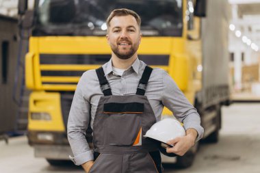 Modüler inşaat endüstrisinde miğfer tutan gülümseyen kamyon şoförünün portresi, lojistik ve ulaşım konsepti