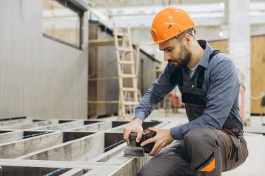 Marangoz, bir modüler yapı fabrikasında prefabrik ev yapımı sırasında elektrikli zımpara makinesi kullanır.