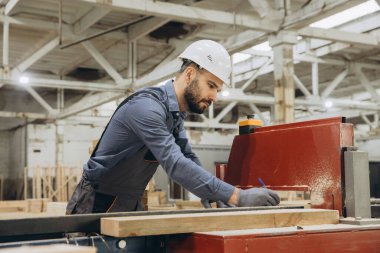 Marangoz ahşap bir kalasın ölçümlerini alıyor prefabrik bir ev fabrikasında üretim hattı üzerinde çalışıyor.