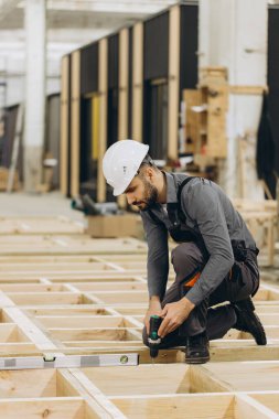 Marangoz, fabrikadaki modüler yapı için prefabrik ahşap panelleri birleştiriyor. Ruh seviyesi ve kablosuz matkap ile hassas hizayı sağlıyor.
