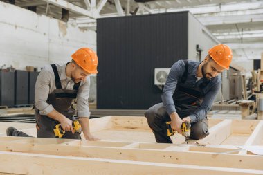 Kablosuz tornavida kullanan iki marangoz fabrikanın içindeki bir modüler bina için prefabrik ahşap bir yapı kuruyor.