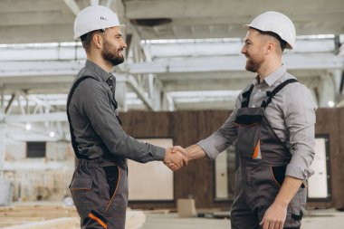 İnşaat işçileri, modern bir fabrikada başarılı bir anlaşma yaptıktan sonra sevinçle el sıkışıyor ve sektörde takım çalışması ve işbirliği sergiliyorlar.