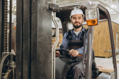Kendine güvenen fabrika işçisi forklift kullanıyor, modüler yapı inşaatında malzeme taşıyor, endüstriyel ortamda verimlilik ve uzmanlık gösteriyor