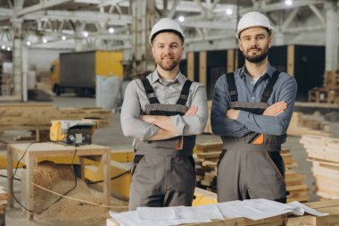 Modüler bir inşaat fabrikasında kesişen iki kendine güvenen inşaat işçisi, prefabrik inşaatlarda takım çalışması ve uzmanlık gösteriyorlar.