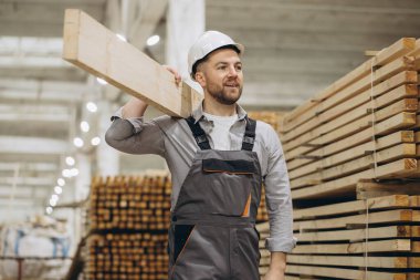 Marangoz, kereste deposunda ahşap kalas taşır. Modüler inşaat endüstrisi.