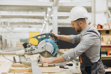 Güvenlik kaskı takan marangoz, modern ve parlak bir marangozluk marangozluğunda tahta kesen dairesel testere kullanıyor.