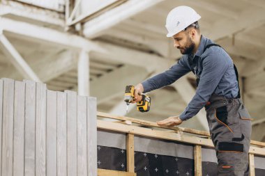İnşaat işçisi inşaat alanında kablosuz tornavida kullanarak prefabrik modüler bina kuruyor.
