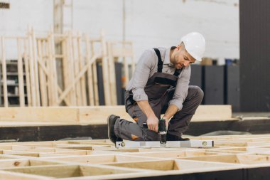 Marangoz ruh seviyesi ve tornavida kullanarak prefabrik ev modülünü monte ediyor, parlak marangozluk atölyesinde ahşap çerçeve üzerinde çalışıyor.