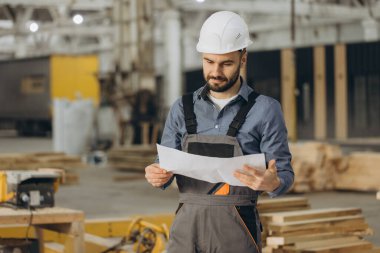 Prefabrik ev fabrikasının planlarını inceleyen inşaat mühendisi, modüler yapı sürecinde kalite ve kesinlik sağlıyor