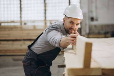 Meşgul fabrikadaki ahşap kirişleri inceleyen marangoz. Kaliteye ve hassasiyete odaklan. İşçi sesleri ve taze ahşap kokusuyla dolu bir atölye. Gelişen modüler ev endüstrisi