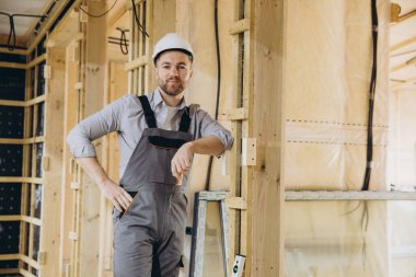 Kendine güvenen inşaat işçisi, inşaat altındaki modüler ahşap binada poz veriyor, gösteri becerileri ve uzmanlığı. Modern, sürdürülebilir tasarım inşaat endüstrisindeki yeniliği yansıtıyor