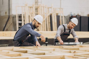 Prefabrik ev panellerini birleştiren iki inşaatçı, elektrikli tornavida ve ruh seviyesini kullanarak, modüler inşa projesi üzerinde çalışıyorlar.