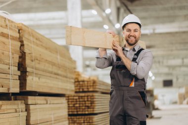 Gülümseyen marangoz, büyük bir kereste deposunda omzunda tahta bir kalas taşıyor.