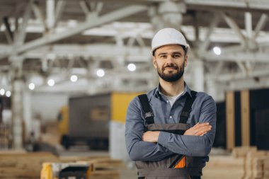 Prefabrik ev fabrikasında çapraz kollu duran kendinden emin inşaat işçisinin portresi.