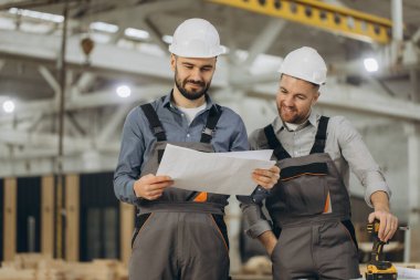 Prefabrik bir ev fabrikasının planlarını inceleyen iki mühendis inşaat projesini tartışıyorlar.