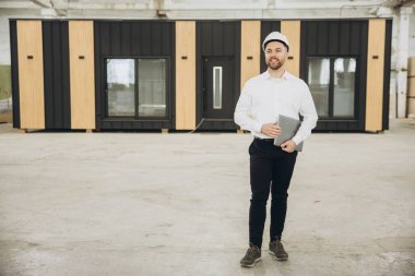 Fabrika, yenilikçi ve sürdürülebilir konut çözümlerinde prefabrik modüler yapı inşaatını denetleyen dizüstü bilgisayar tutan mimar