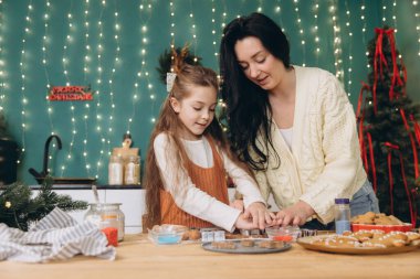 Anne ve kızı, güzel dekore edilmiş mutfaklarında birlikte Noel kurabiyeleri pişiriyor, tatlı anılar yaratıyor ve şenlikli hediyeler hazırlıyorlar.