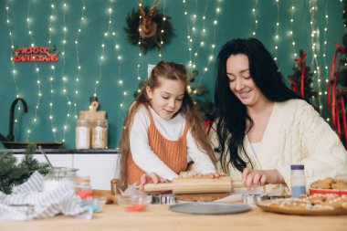 Anne ve kızı neşeli bir şekilde merdaneyle Noel neşesiyle dolu güzel dekore edilmiş bir mutfakta şenlikli kurabiyeler yapıyorlar.