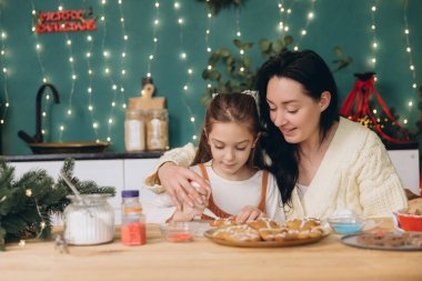 Anne ve kızı, Noel 'de Noel kurabiyelerini Noel ışıklarıyla süslemenin keyfini çıkarıyorlar.