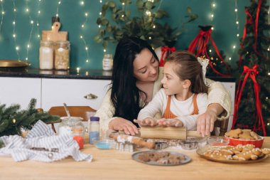 Anne ve kızı Noel için zencefilli kurabiye hazırlıyorlar. Süslü bir mutfakta merdane ve kurabiye keskisi kullanıyorlar.