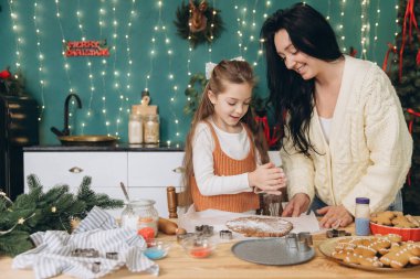 Anne ve kızı kurabiye hamurunun üzerine un saçıyor, süslenmiş mutfaklarında Noel kurabiyeleri yapmaya hazırlanıyorlar.