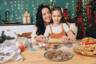 Anne ve kızı, güzel dekore edilmiş bir mutfakta birlikte Noel kurabiyesi pişiriyor ve uzun süreli tatil anıları yaratıyorlar.