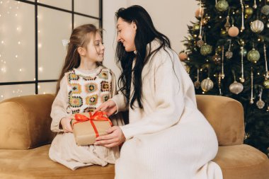 Anne ve kızı süslenmiş ağacın yanındaki koltukta otururken Noel hediyelerini değiş tokuş ediyorlar.
