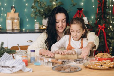 Anne ve kız hamuru ahşap oklavayla yuvarlıyor, Noel için zencefilli kurabiye pişiriyor.