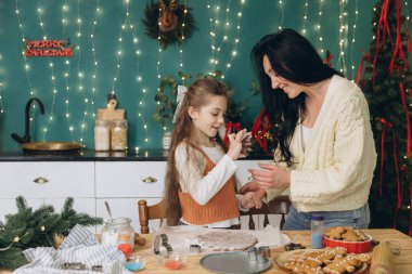 Anne ve kızı, Noel kurabiyelerini neşe içinde pişiriyorlar. Güzel dekore edilmiş mutfaklarında, bayram geleneklerini kucaklıyorlar.