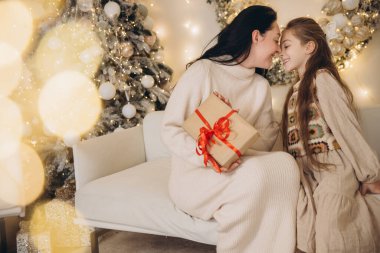 Anne ve kızı Noel hediyelerini paylaşırken, dekore edilmiş bir oturma odasındaki kanepede otururken,