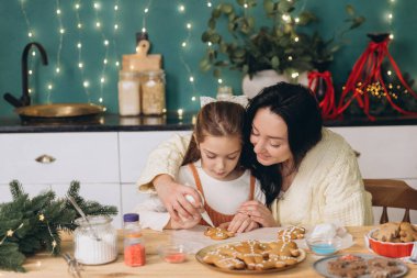 Anne ve kızı, sıcak bir Noel süslemesinde zencefilli kurabiyeleri birlikte dekore ediyorlar.