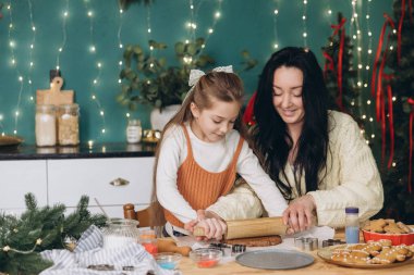 Anne ve kız hamuru ahşap oklavayla yuvarlıyor, Noel kurabiyeleri yapıyor, süslenmiş mutfakta.