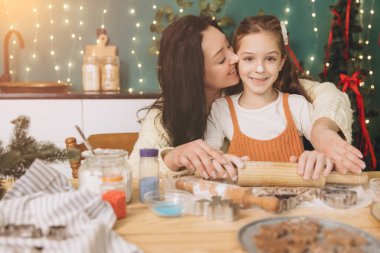 Anne kızını öperken birlikte Noel kurabiyeleri hazırlıyor sıcak, şenlikli bir mutfakta sevgi dolu anılar yaratıyor.