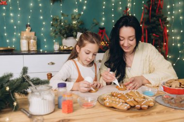 Anne ve kızı Noel için dekore edilmiş bir mutfakta zencefilli kurabiye süslüyor.