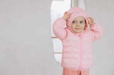 Pembe kışlık ceket giyen sevimli bir kız çocuğu, kaputu şakayla ayarlıyor, sıcaklık ve mutluluk saçıyor.