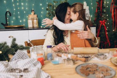 Güzel dekore edilmiş bir mutfakta birlikte Noel kurabiyeleri hazırlarken anne ve kızı sıcak bir kucaklaşmayı paylaşıyorlar.