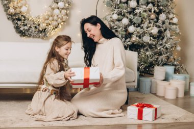 Anne ve kızı Noel hediyelerini dekore edilmiş ağaç ve kanepenin yanında değiş tokuş ediyorlar, birlikte Noel 'in tadını çıkarıyorlar.