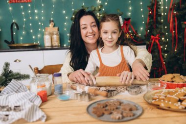 Güzel dekore edilmiş bir mutfakta Noel kurabiyeleri pişirirken gülümseyen anne ve kız neşeli anılar yaratıyor.