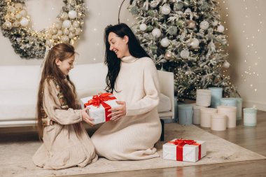 Anne ve kızı Noel ağacının yanında Noel hediyelerini değiş tokuş ediyorlar, sıcak bir aile kutlaması yapıyorlar.