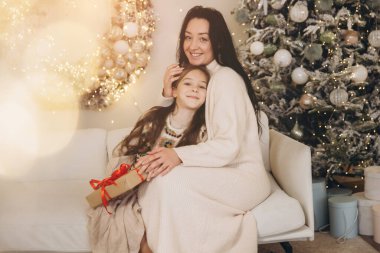 Anne ve kızı, Noel günü, Noel ağacının yanındaki bir kanepede oturarak hassas bir anı paylaşıyorlar.