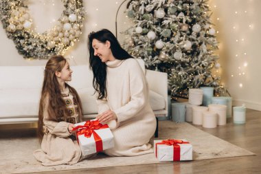 Anne ve kızı Noel hediyelerini dekore edilmiş ağacın yanında değiş tokuş ediyorlar, birlikte Noel 'in tadını çıkarıyorlar.