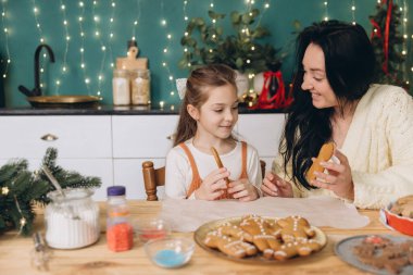 Anne ve kızı Noel için dekore edilmiş bir mutfakta zencefilli kurabiye süslüyor.