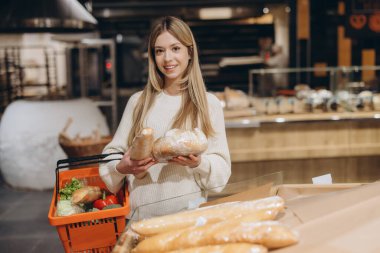 Müşteri, elinde alışveriş sepeti olan bir süpermarketten taze ekmek ve ekmek seçiyor.